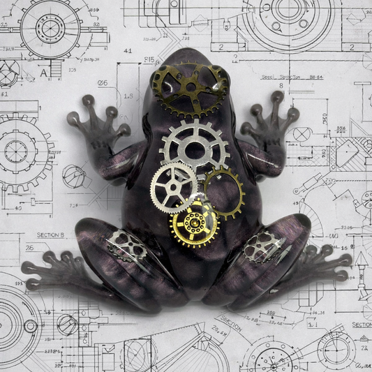A dark purple frog ornament decorated with metal gears, set against a background of technical blueprints. The gears are in shades of gold and silver, creating a steampunk aesthetic. The frog is in a relaxed pose.