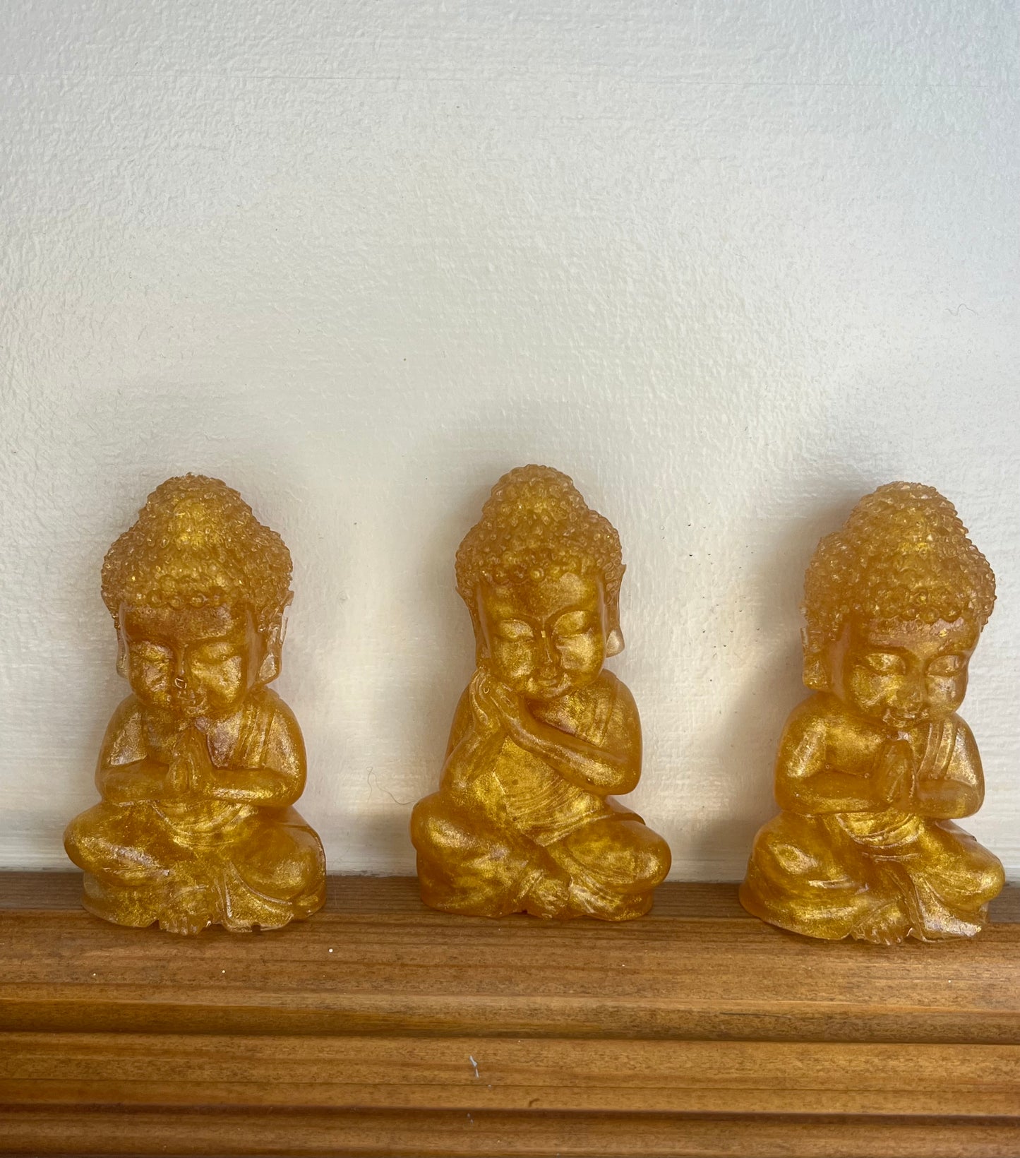 3 golden coloured resin Thai Buddha figures in different poses on a wooden shelf.