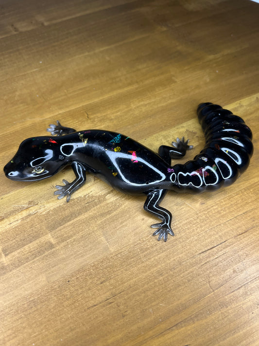 Glossy black resin salamander with colourful embedded glitter accents, displayed on a wooden surface.