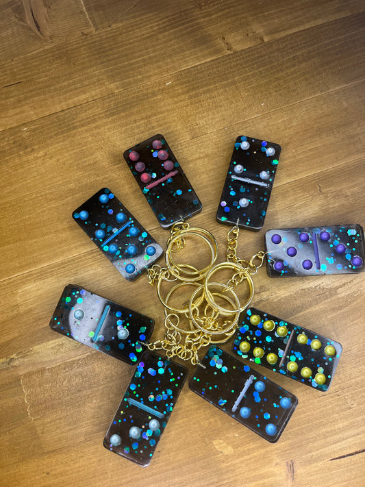 Collection of black and green glitter domino keyrings with gold chains on a wooden surface