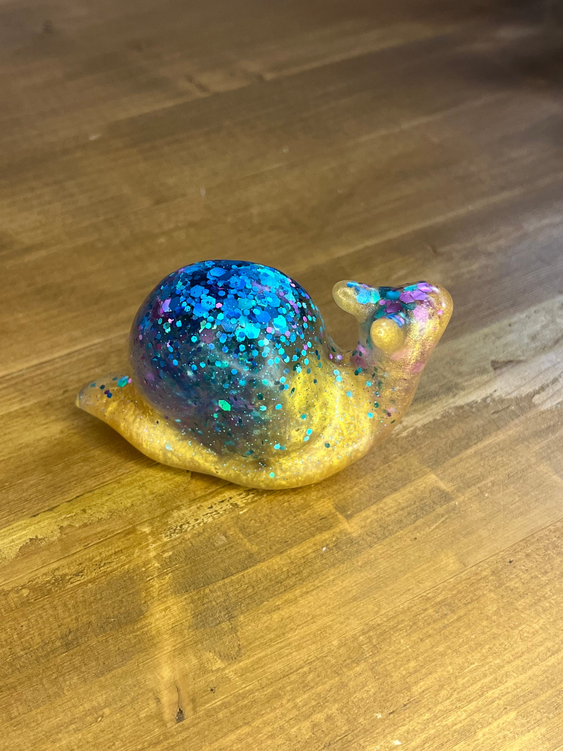 Decorative figurine of a snail with glittery blue body on a wooden surface