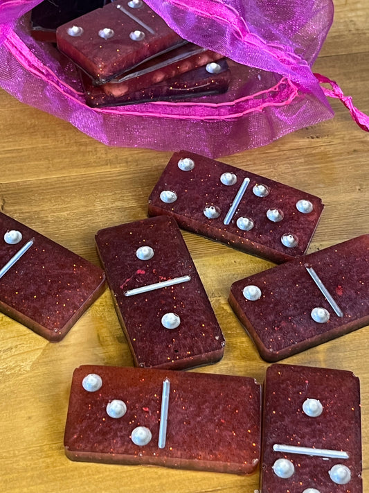 Sparkling red dominoes with white dots on a wooden surface, some in a pink bag.