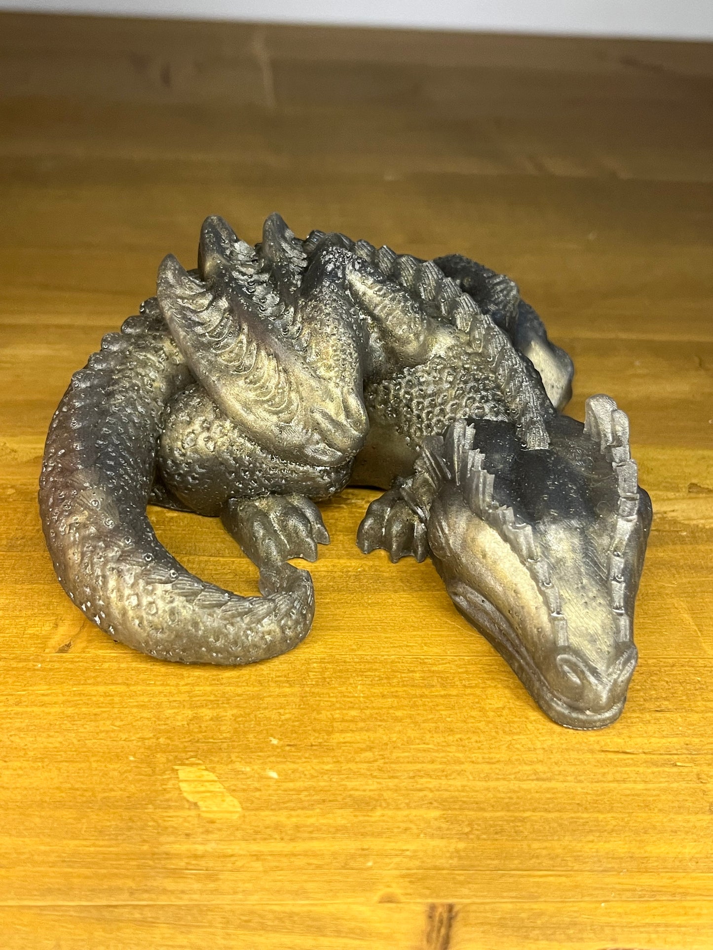 Gold resin sleeping dragon, curled up on a wooden shelf