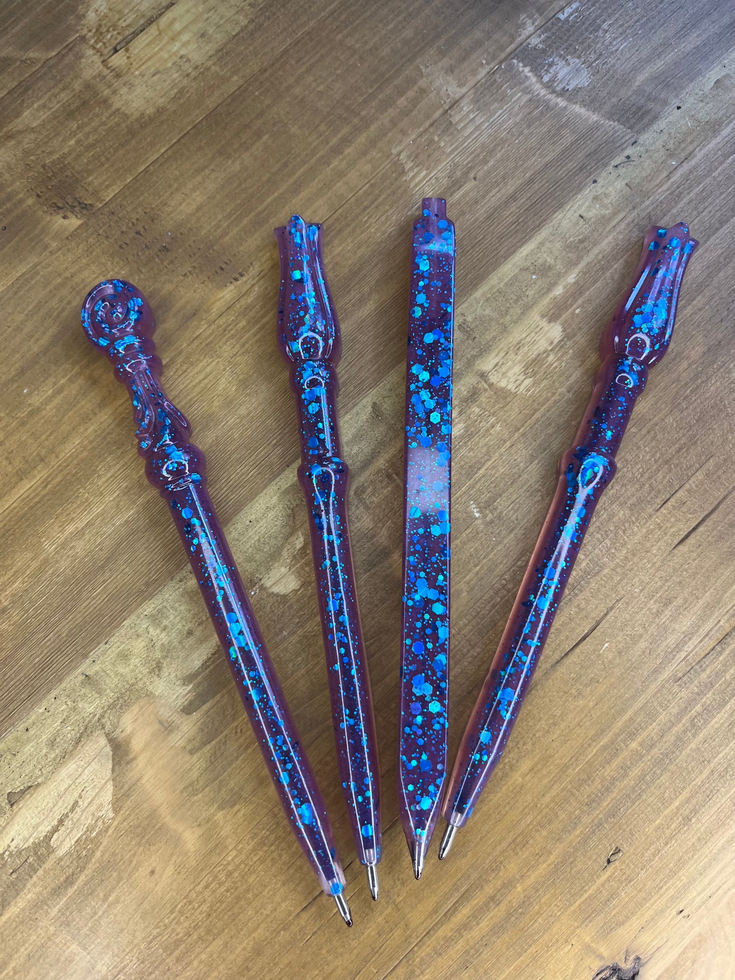 Four decorative wand shaped pens with a blue and purple speckled pattern on a wooden surface.