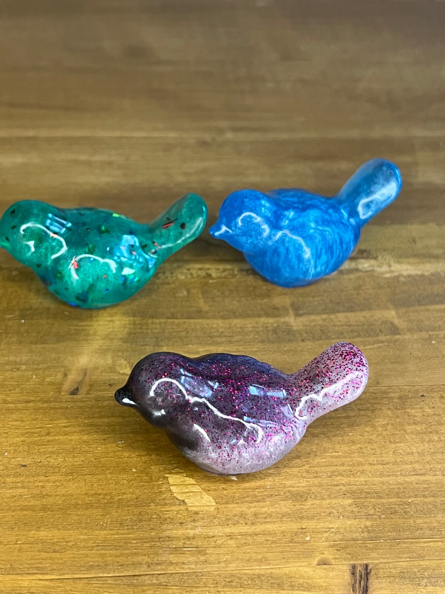 Three colorful resin bird figurines on a wooden surface