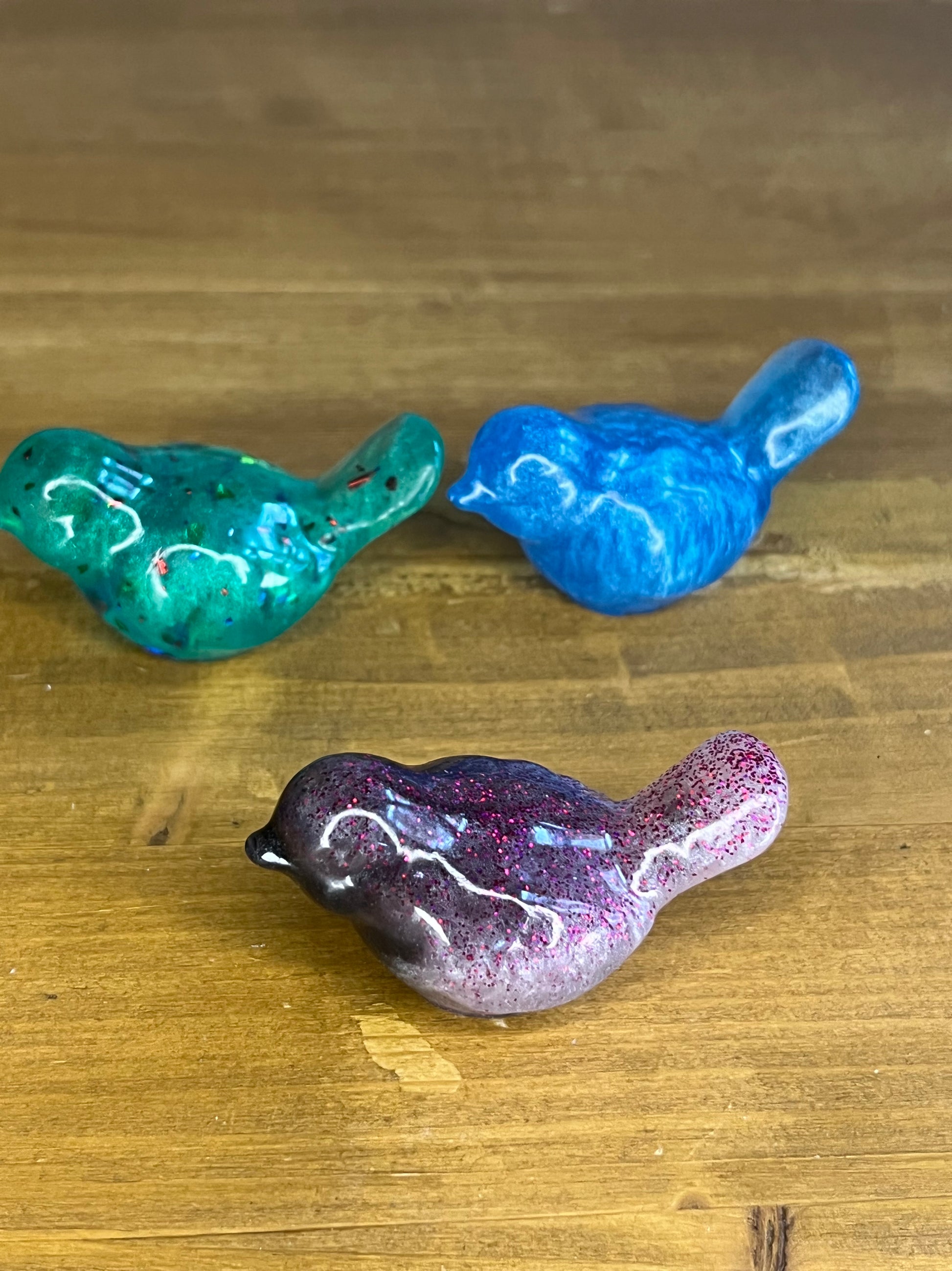 Three colorful resin bird figurines on a wooden surface