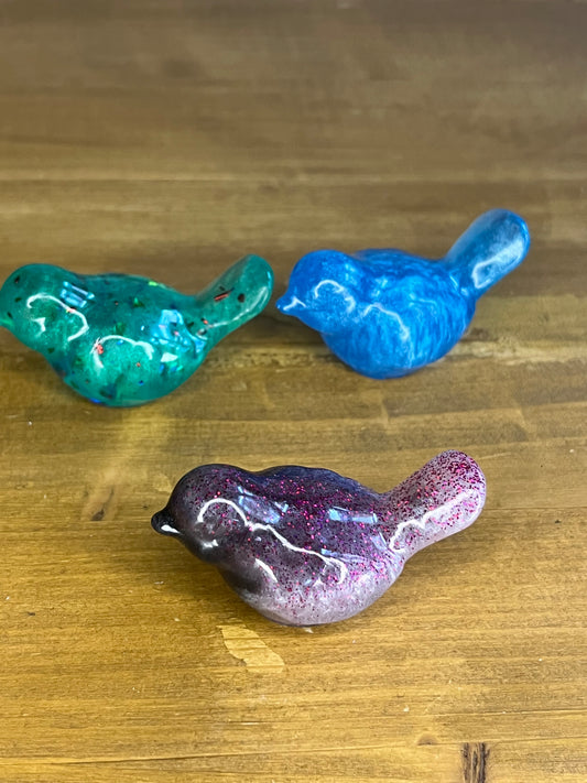 Three colorful resin bird figurines on a wooden surface
