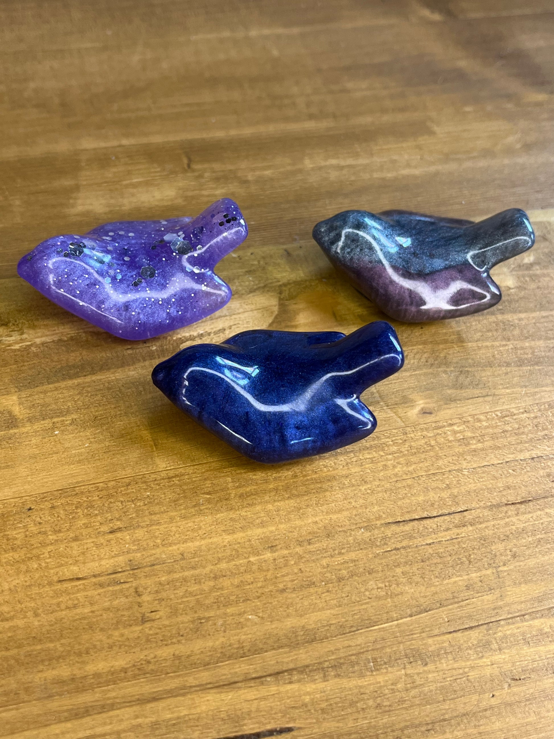 Three purple and blue resin birds on a wooden surface