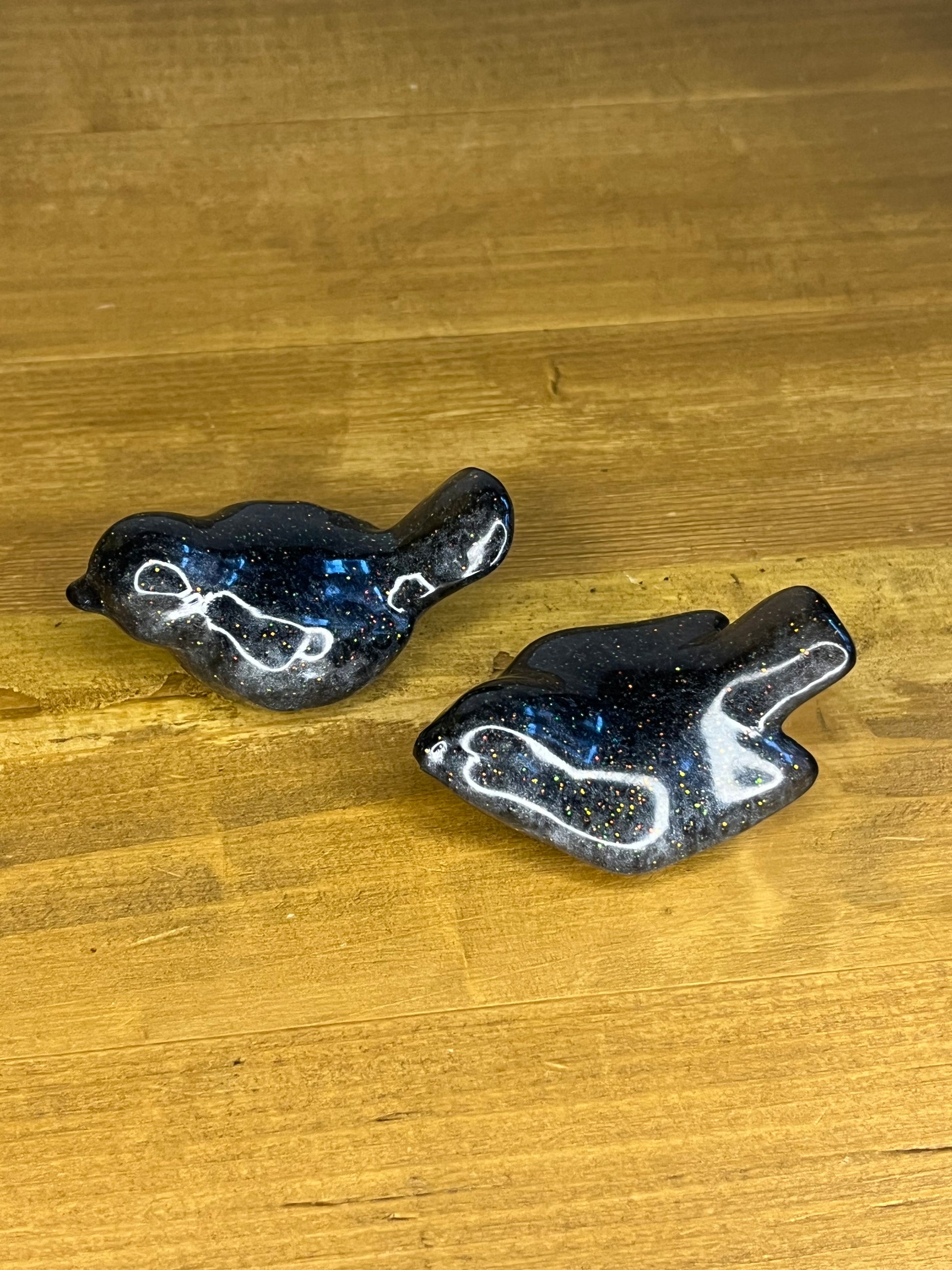 Two black and silver resin bird figurines
 on a wooden surface