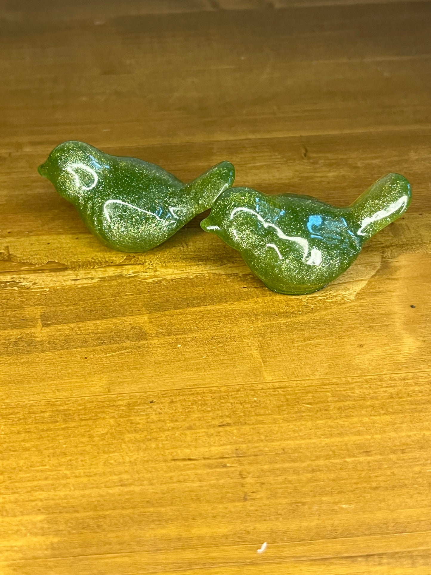 2 Green glittery resin bird figurines on a wooden surface
