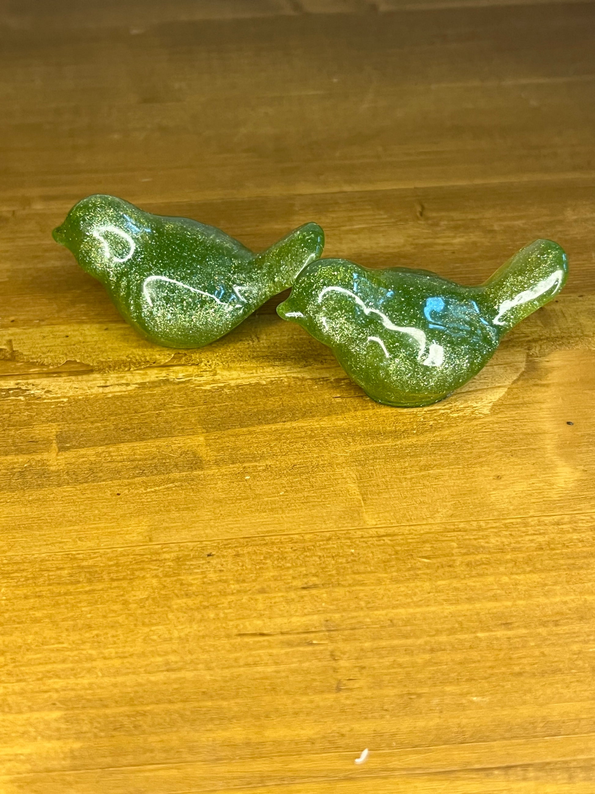 2 Green glittery resin bird figurines on a wooden surface