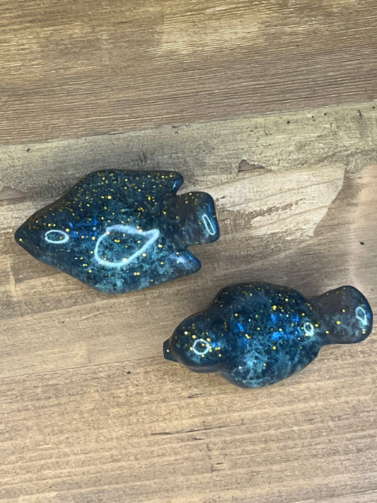 Two blue/green resin bird figurines on a wooden surface
