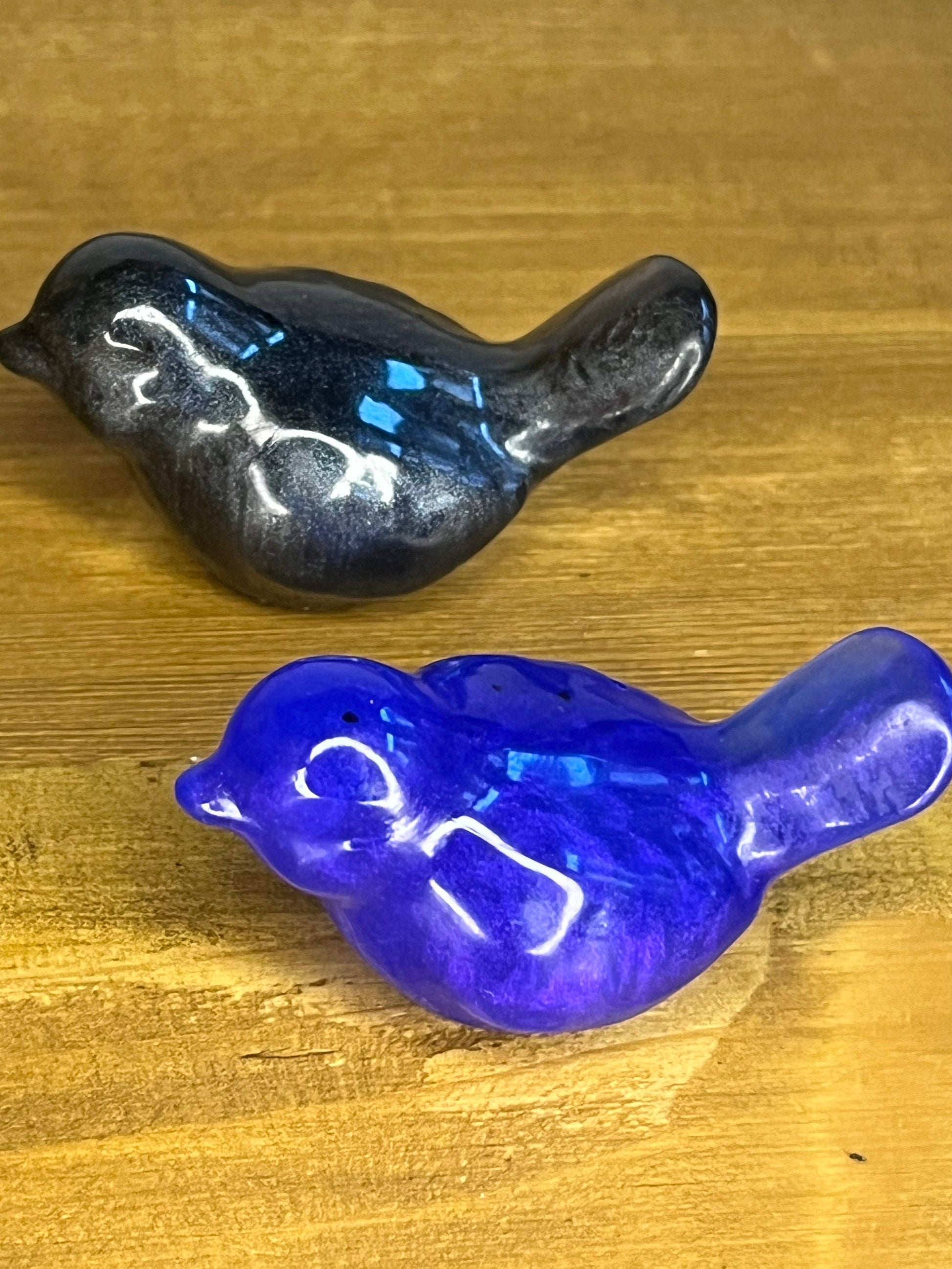 Two resin bird figurines, one black and one blue, on a wooden surface.