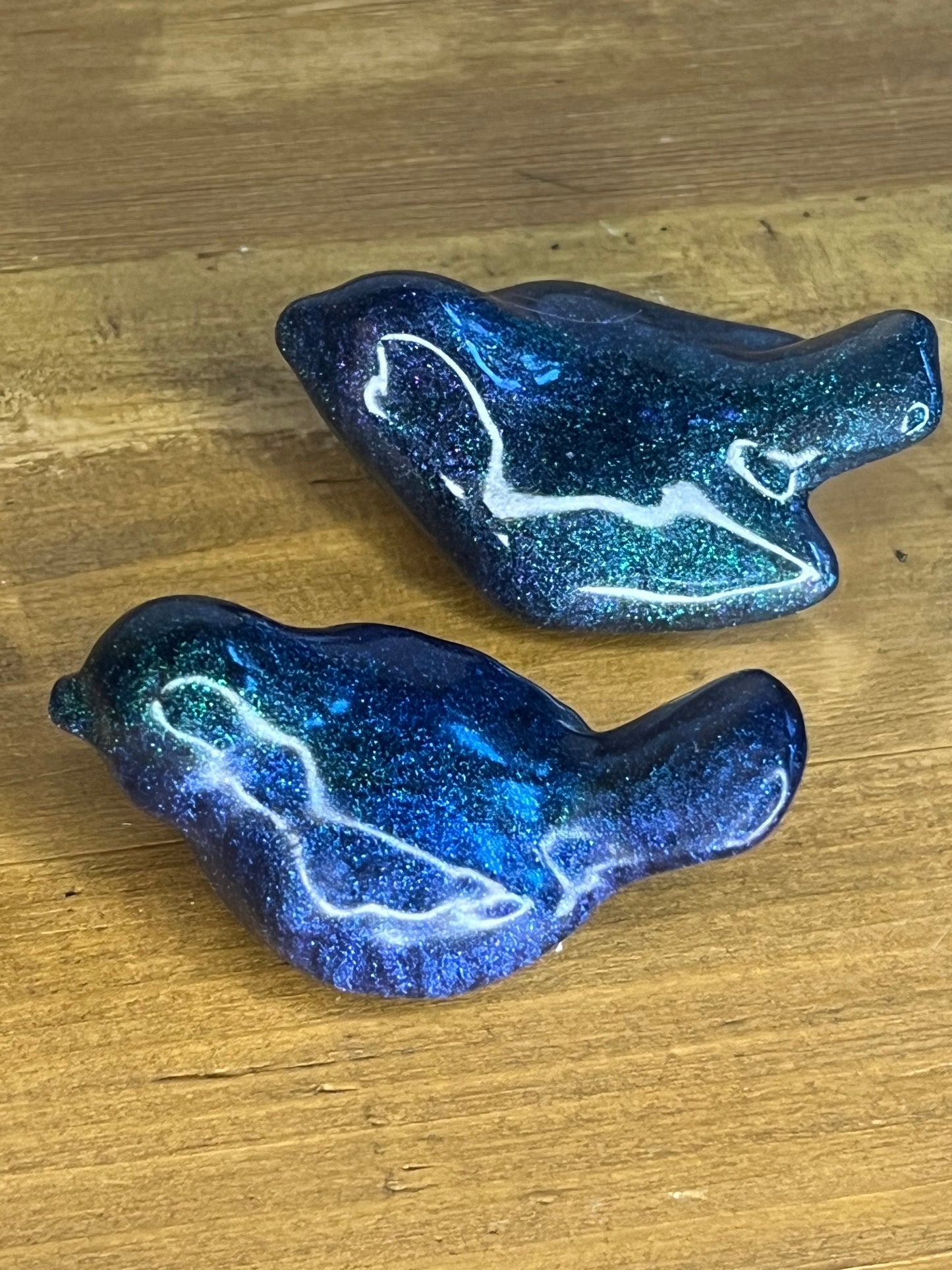 Two blue glittery resin birds on a wooden surface