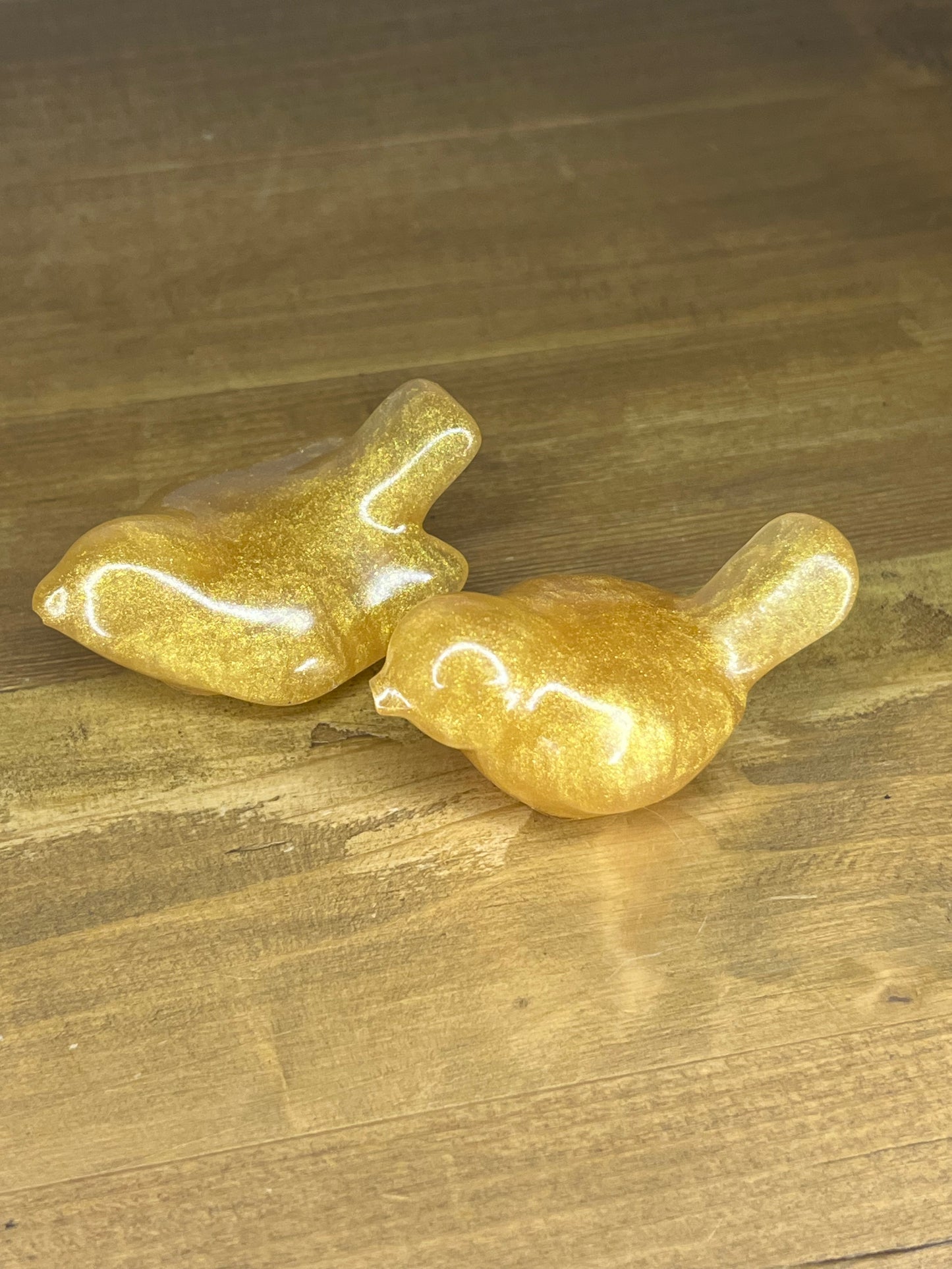 Two gold-colored resin bird figurines
on a wooden surface