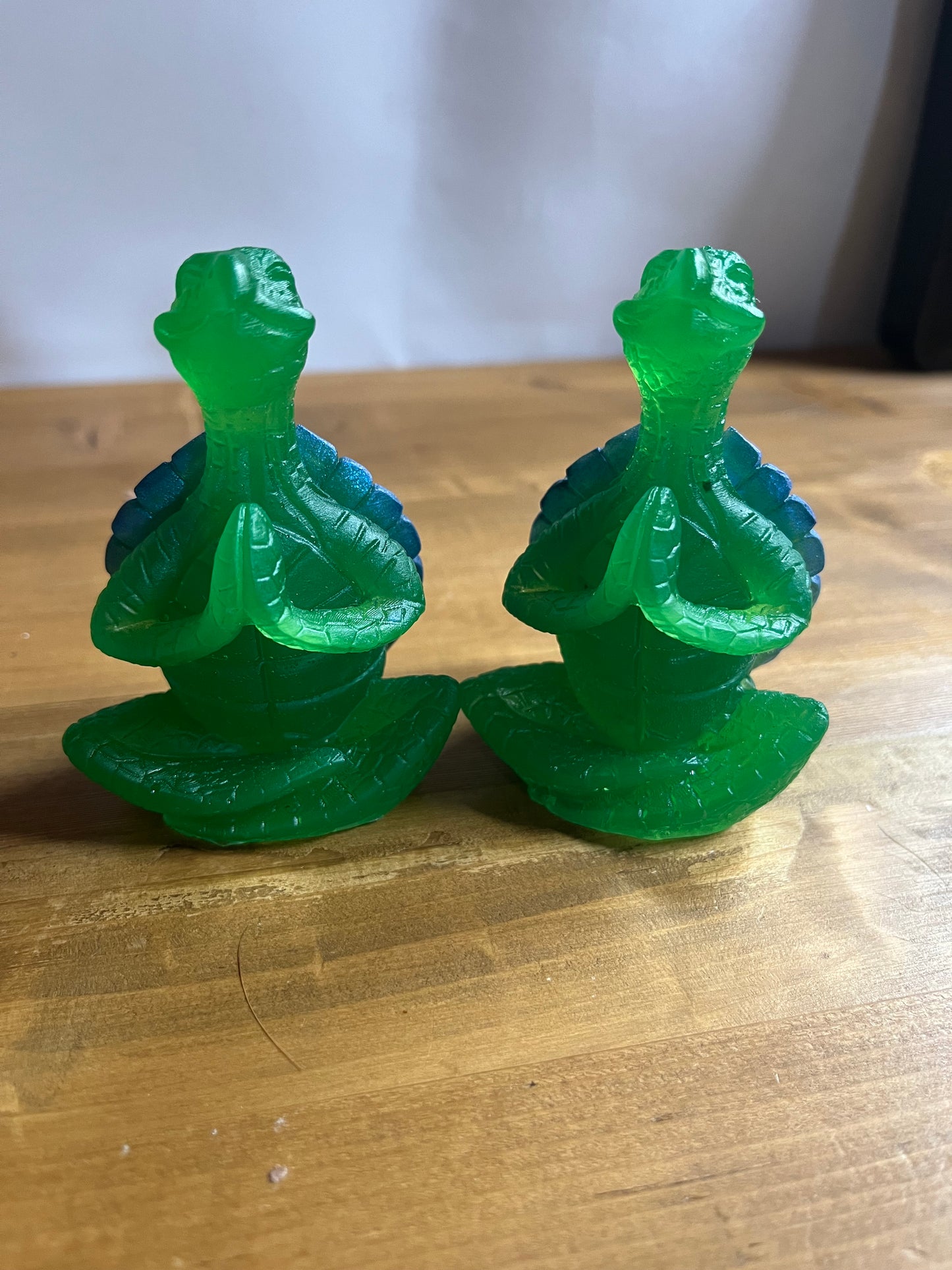 Two green resin turtles  in a lotus pose on a wooden surface