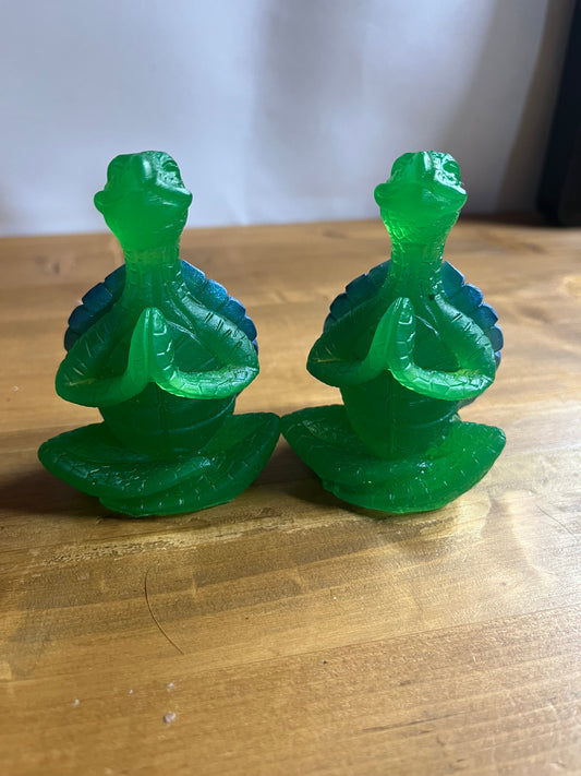 Two green resin turtles  in a lotus pose on a wooden surface