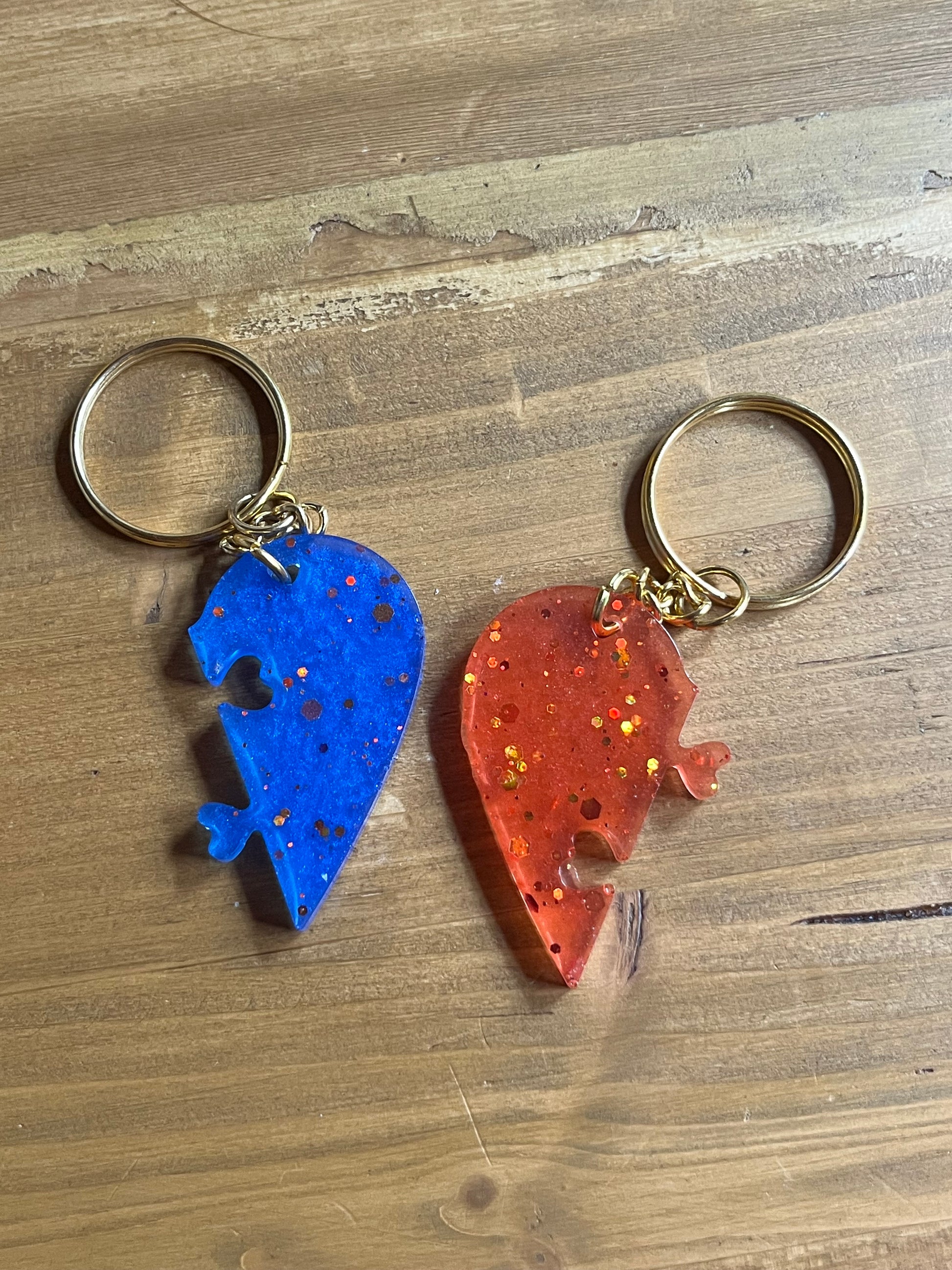 Two keychains shaped like a red half heart and blue matching half heart on a wooden surface.