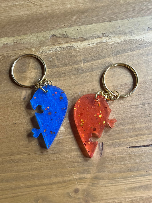 Two keychains shaped like a red half heart and blue matching half heart on a wooden surface.