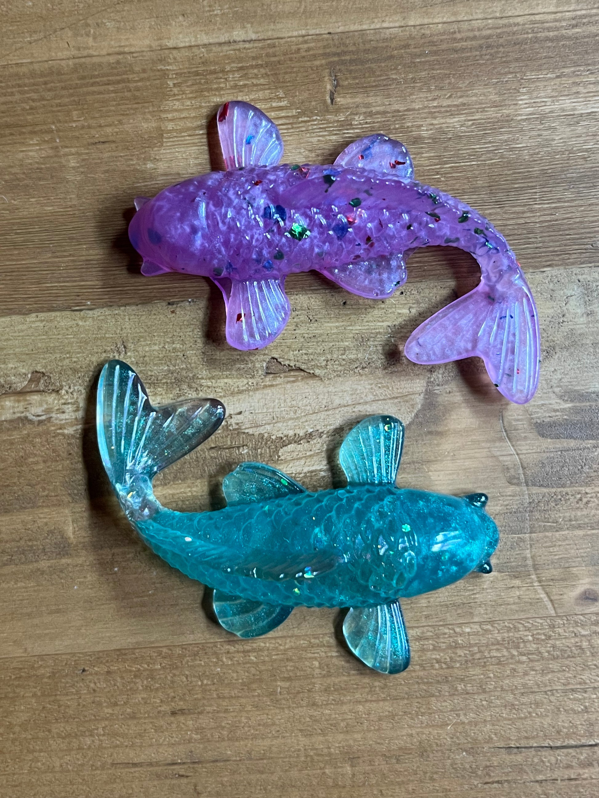 Two resin fish figures, one pink and one green, on a wooden surface.