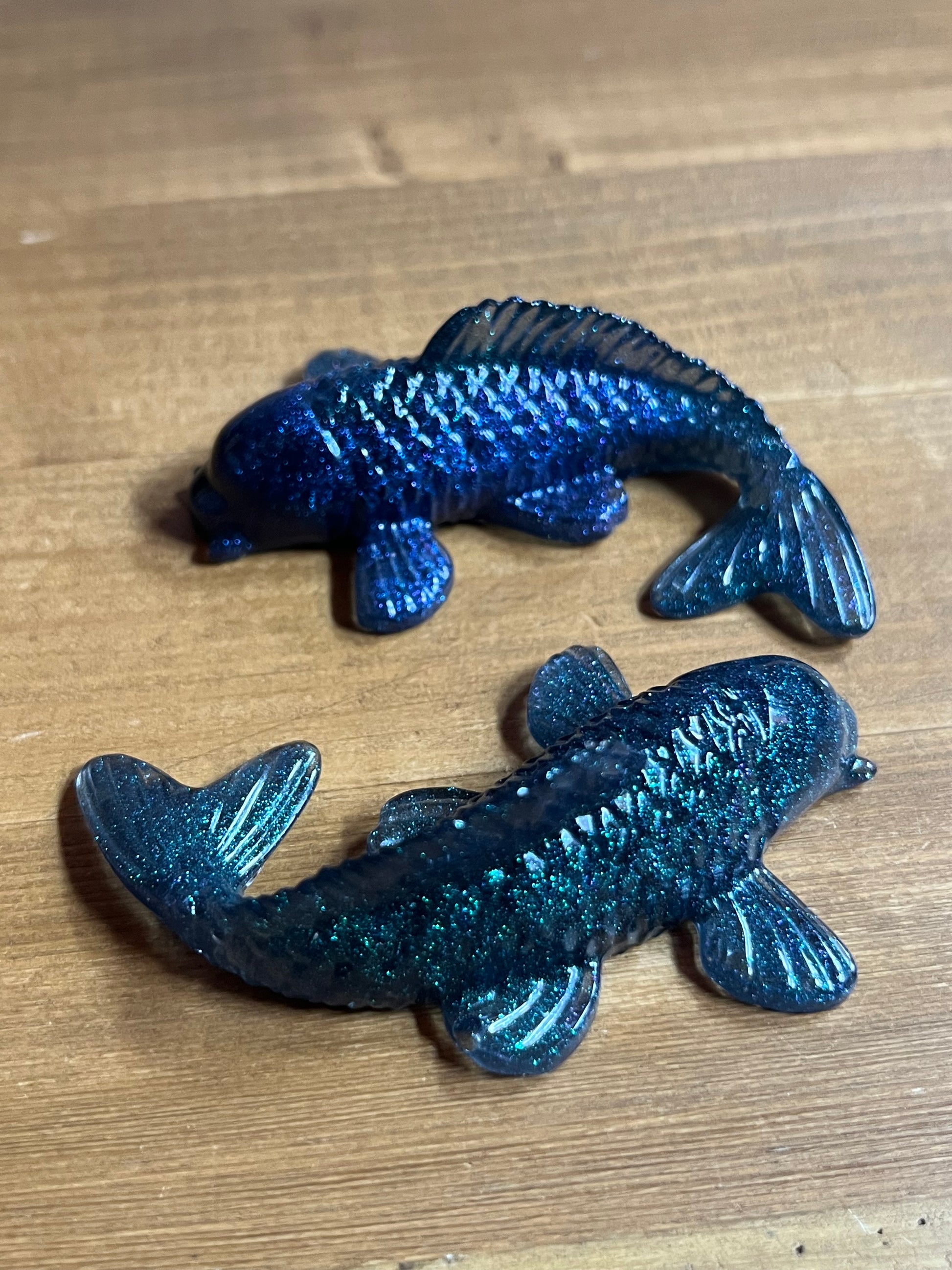 Two blue glittery fish-shaped objects on a wooden surface
