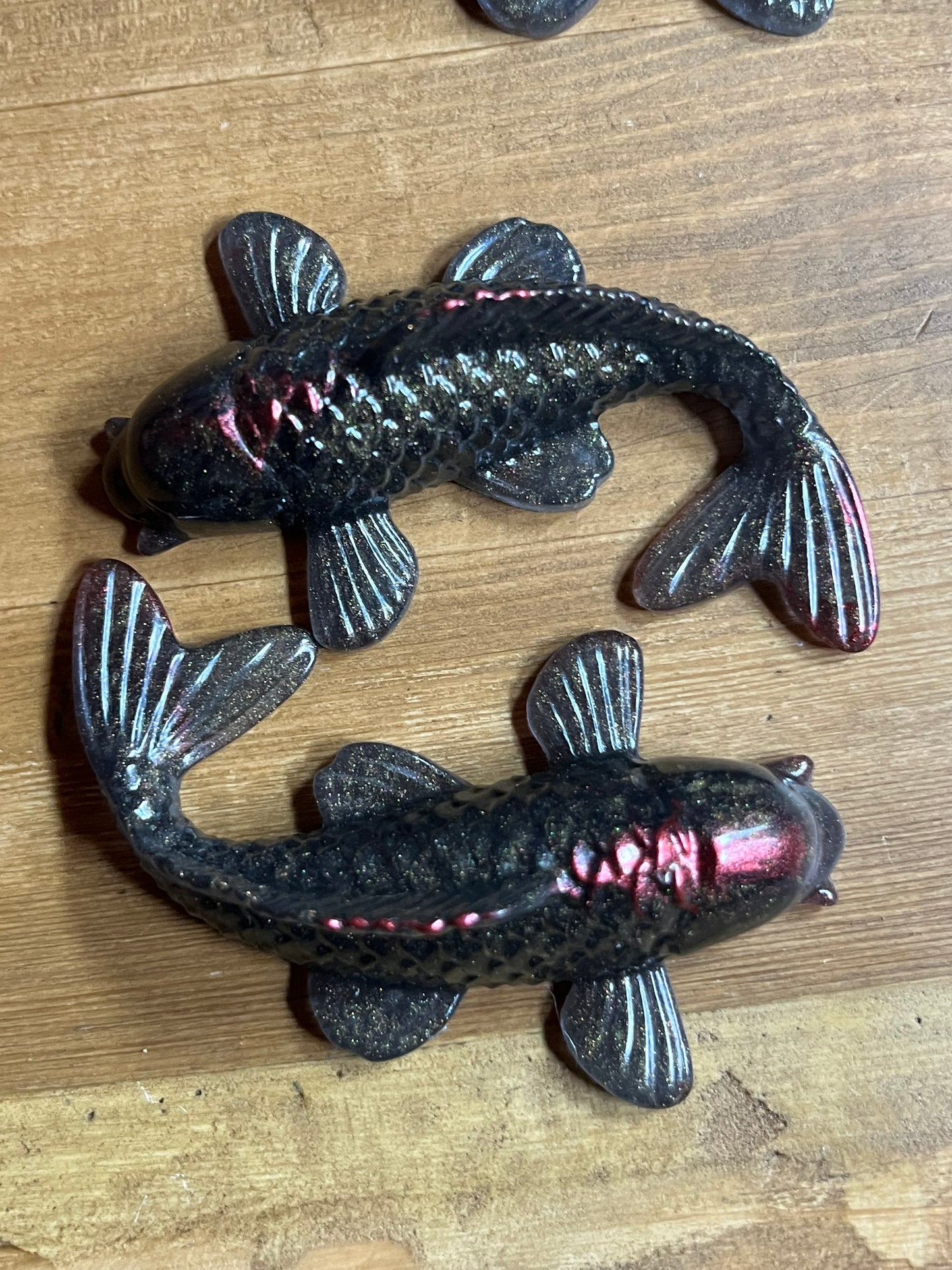 Two metallic looking resin fish figures on a wooden surface