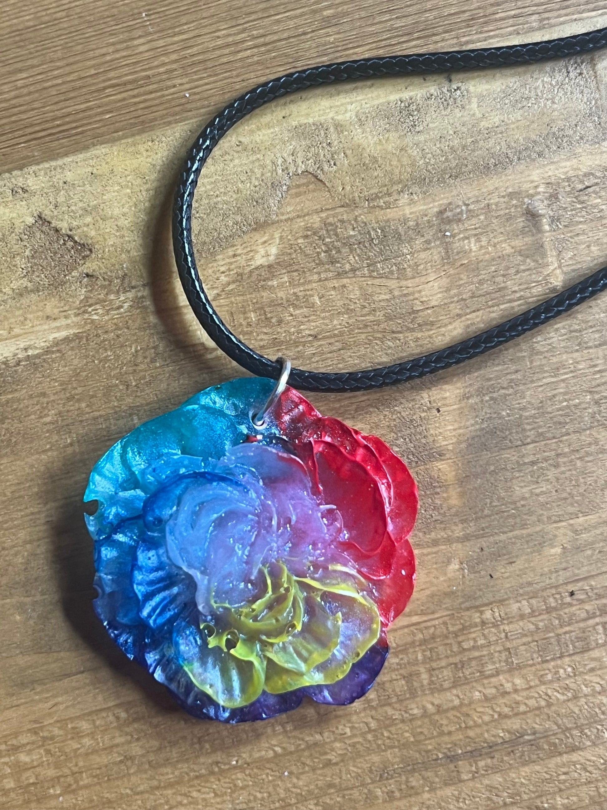 Colorful flower-shaped pendant on a black cord against a wooden background