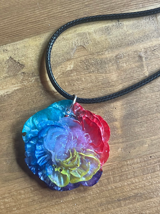 Colorful flower-shaped pendant on a black cord against a wooden background