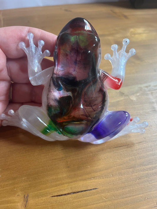 Colorful resin frog sculpture held in a hand on a wooden surface