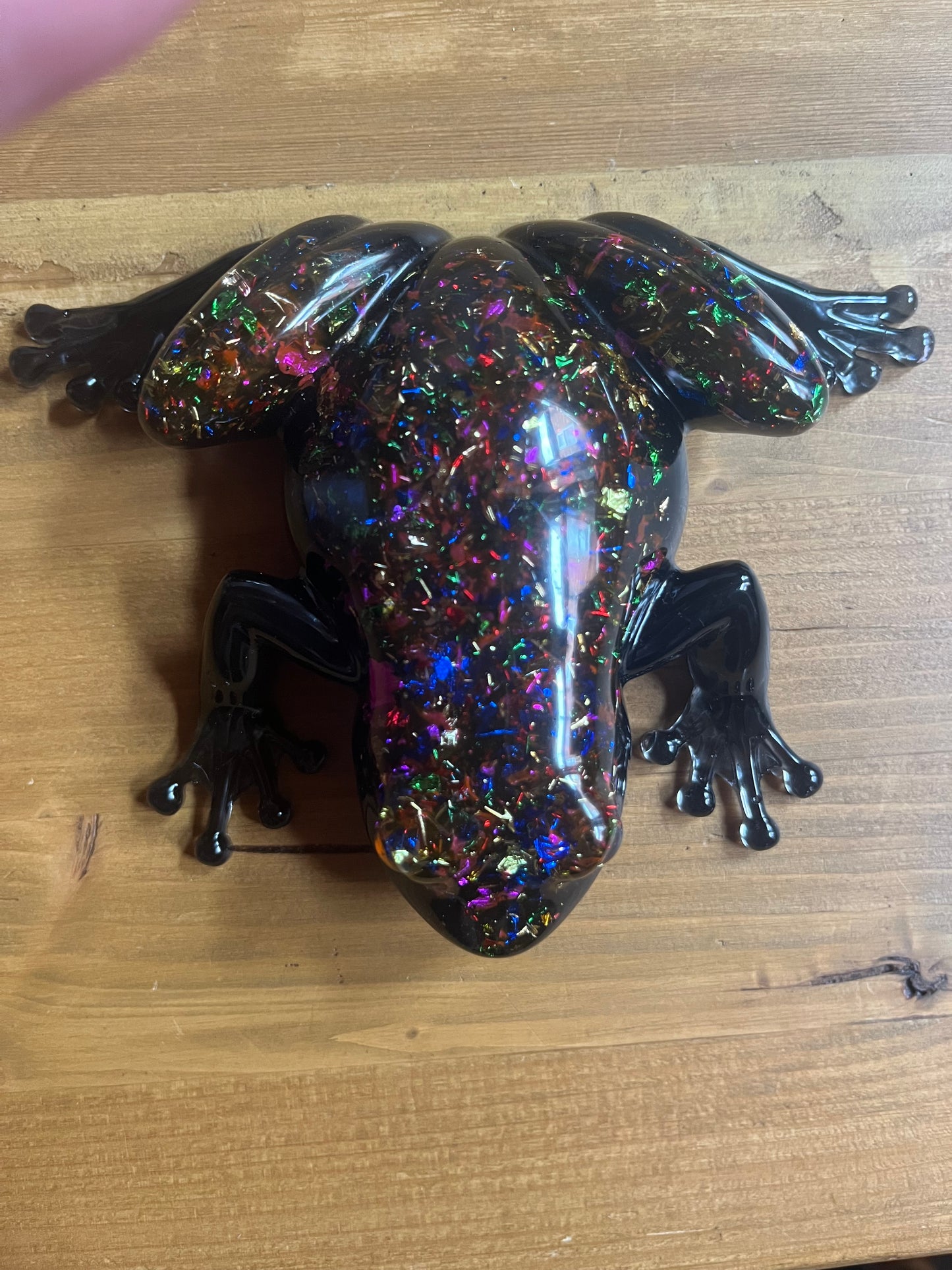 Multicolored glittery frog figurine on a wooden surface