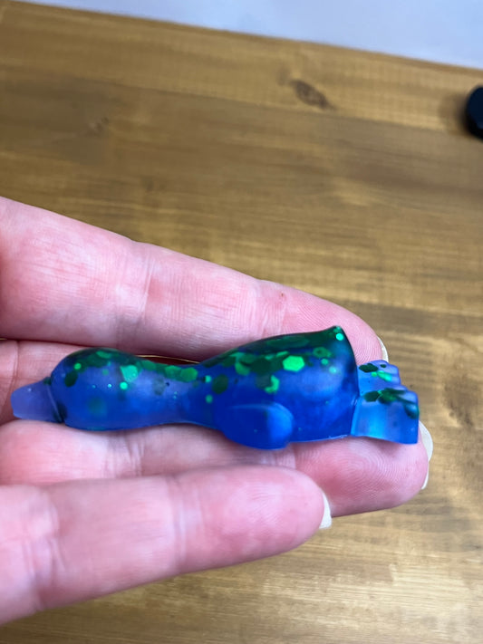 A small translucent blue and green decorative duck held between fingers over a wooden tabletop.