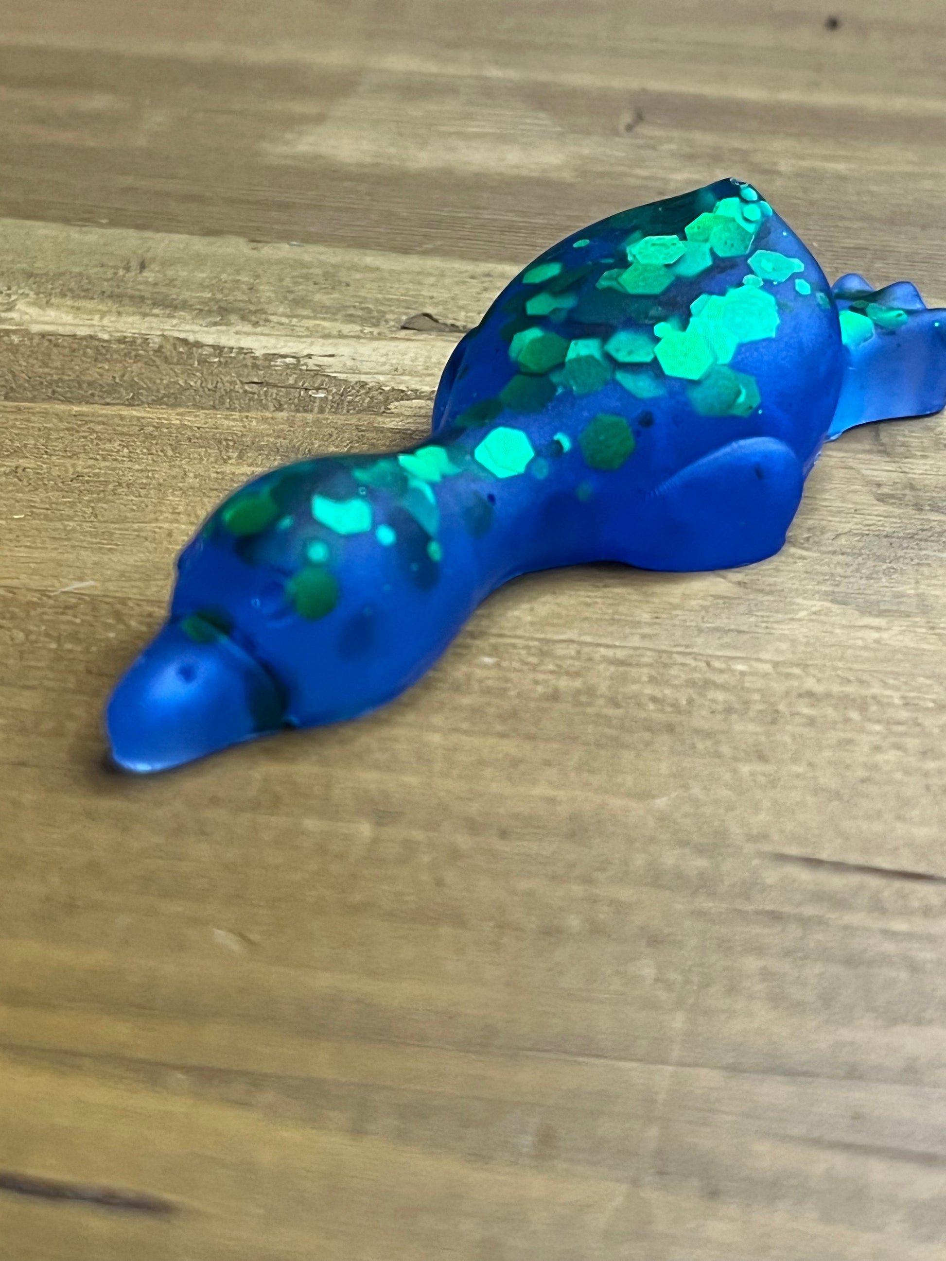 A blue translucent duck-shaped object with green glittery spots, photographed on a wooden surface.