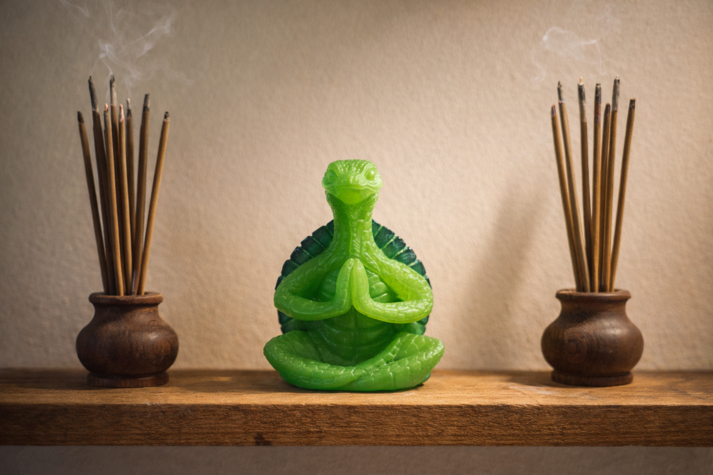 Green turtle-shaped figurine with two wooden incense sticks holders on a wooden shelf.